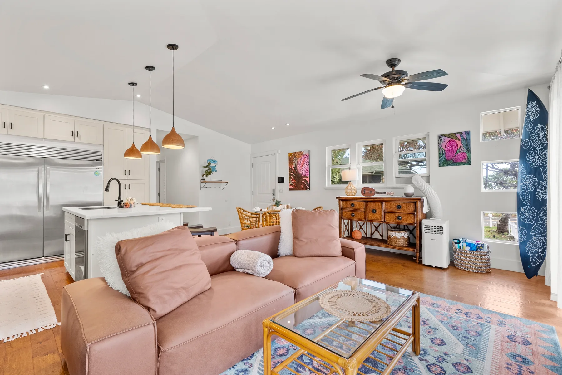 A bright living room with a pink seating area, glass coffee table, and colorful wall art.