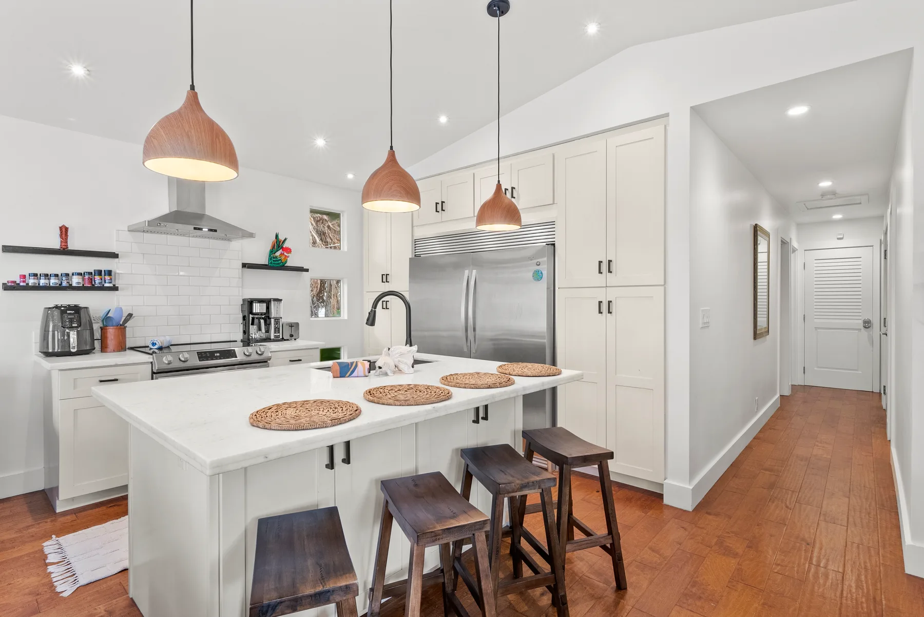 Una cocina luminosa con una isla grande, lámparas colgantes y electrodomésticos de acero inoxidable.