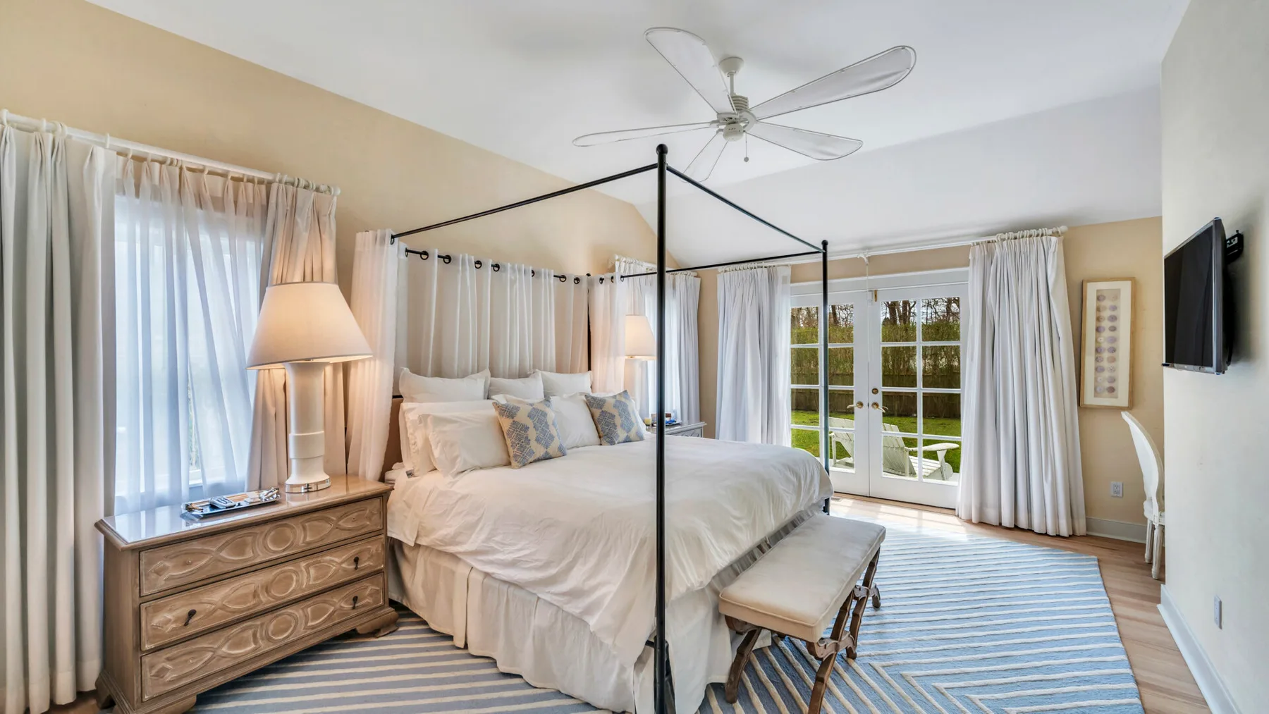 A bedroom with a canopy bed, bedside dresser, and windows covered by curtains.