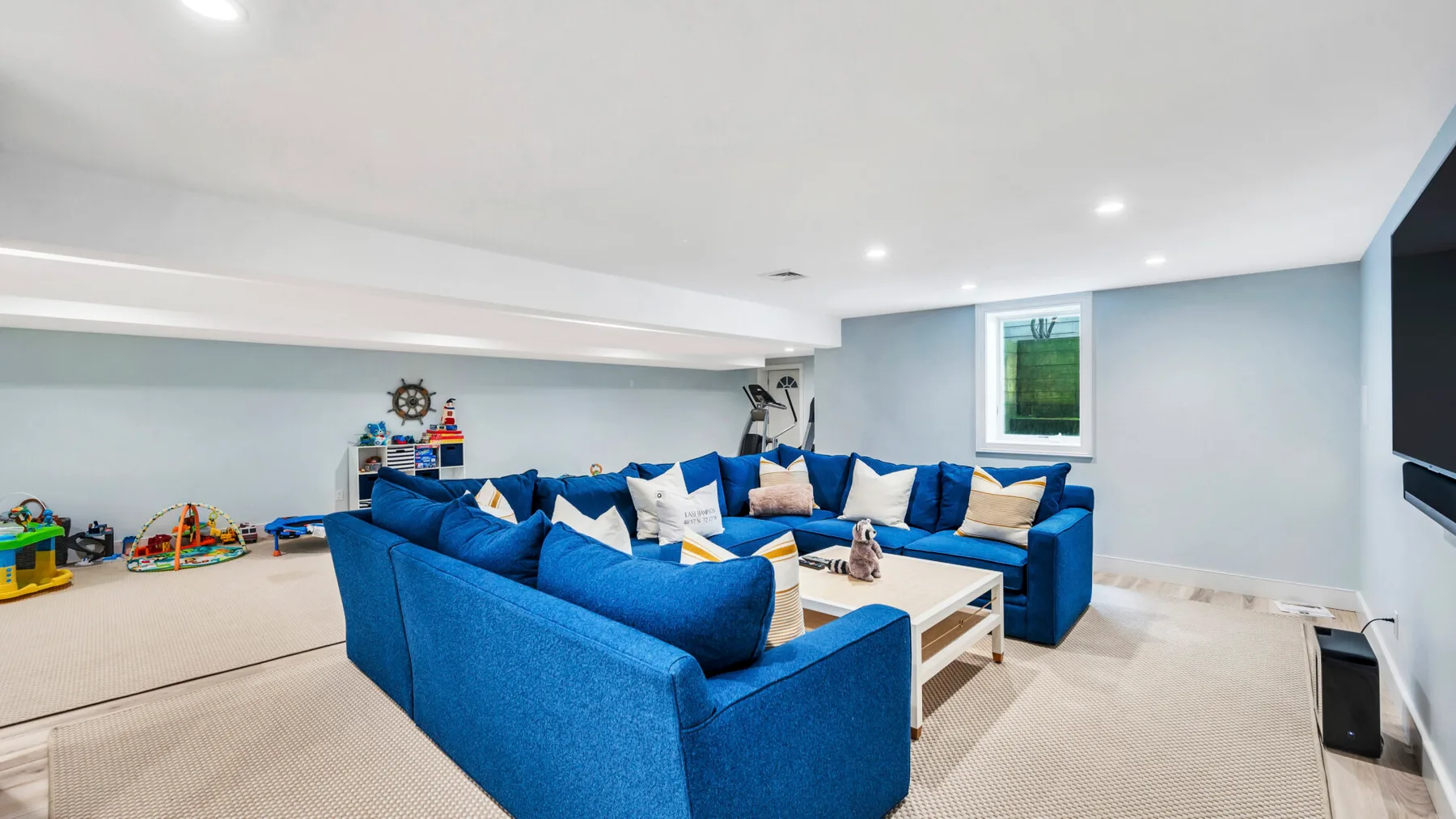 A basement-style lounge with blue seating arranged around a low coffee table.