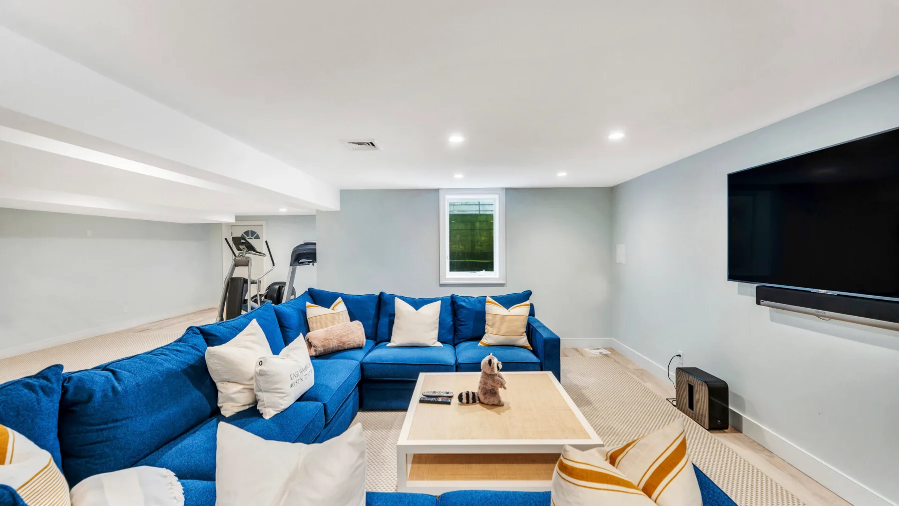 A basement living room with blue seating, a coffee table, and a wall-mounted television.