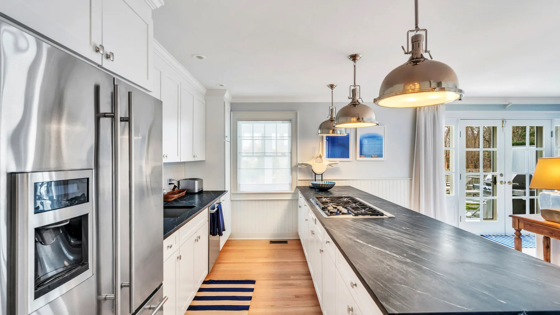 A bright kitchen with a long island, stainless steel refrigerator, and pendant lights.