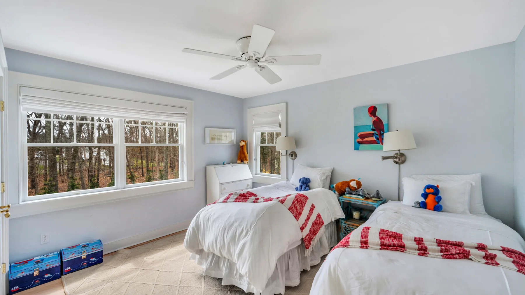 A bright bedroom with two beds and large windows overlooking trees.