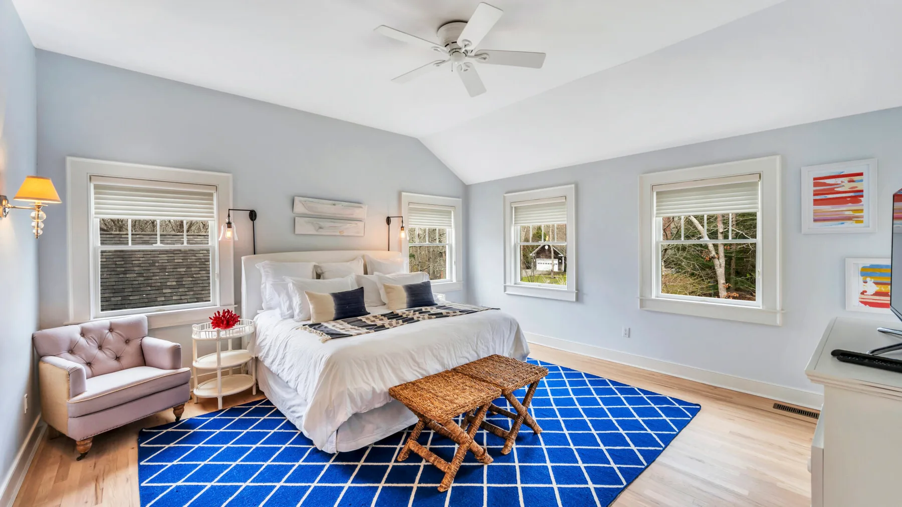 A bright bedroom with a white bed, blue rug, and windows.