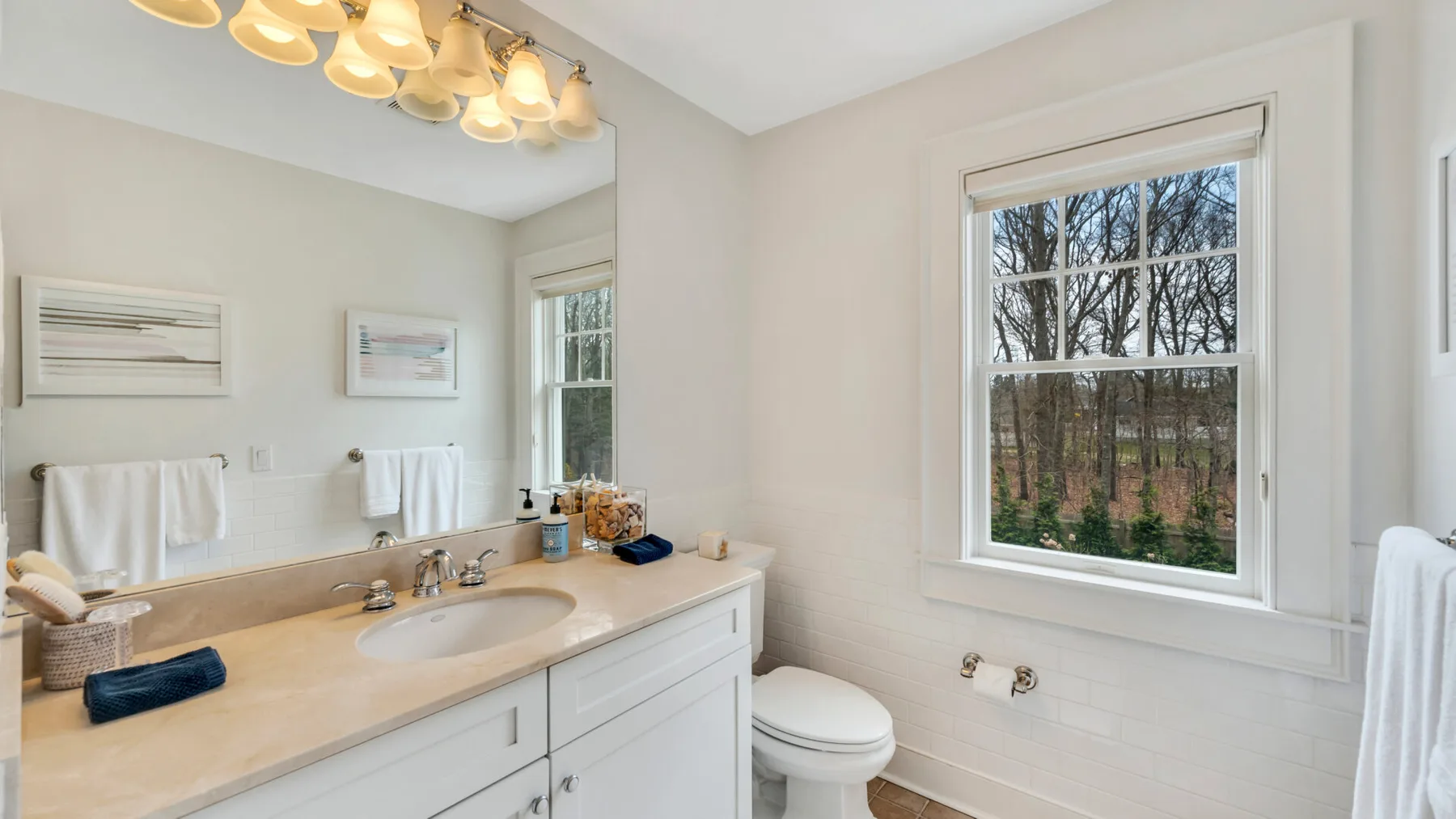 A bright bathroom with a long vanity, mirror, toilet, and window.