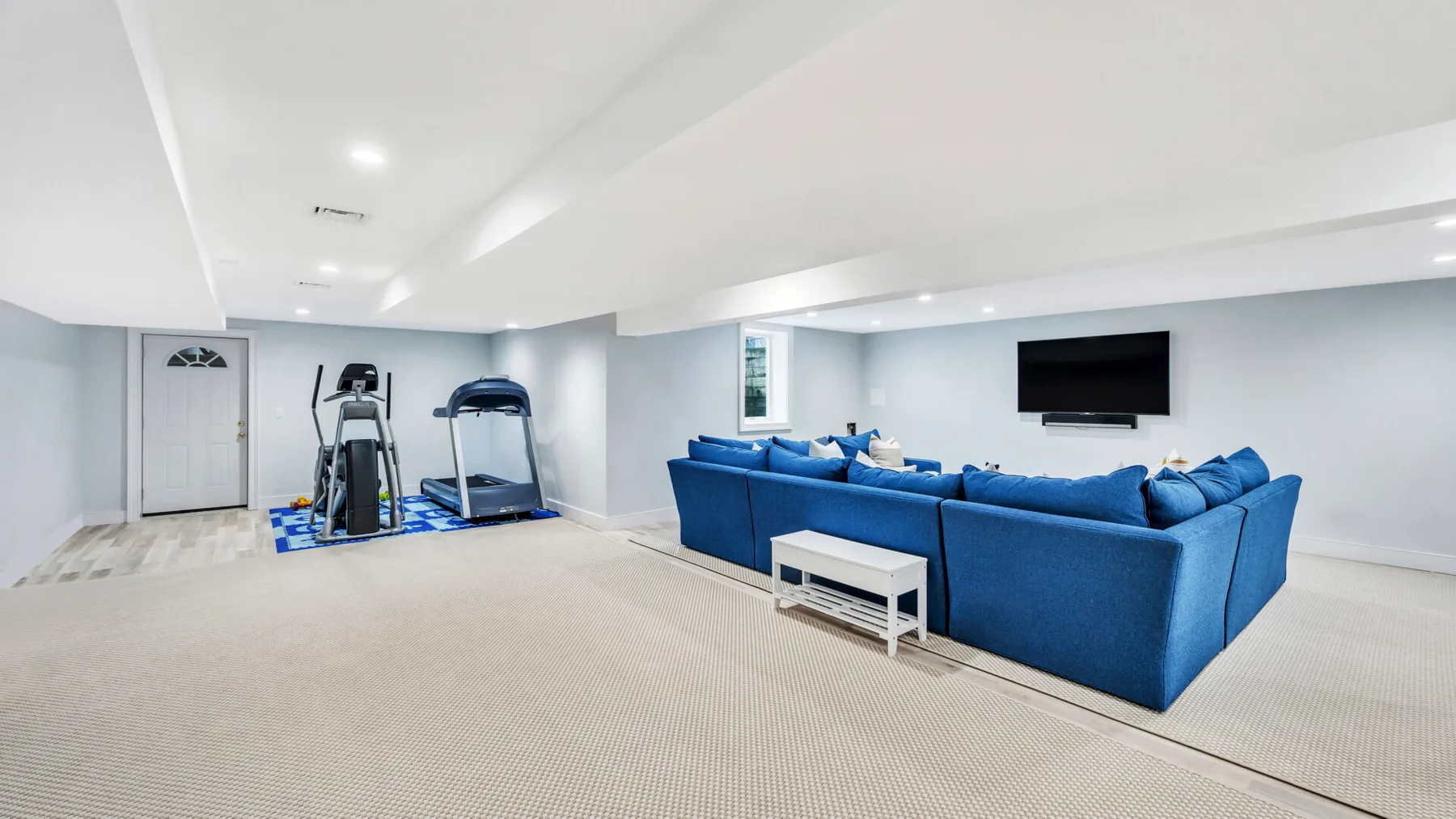 A finished basement lounge with blue seating and exercise equipment.