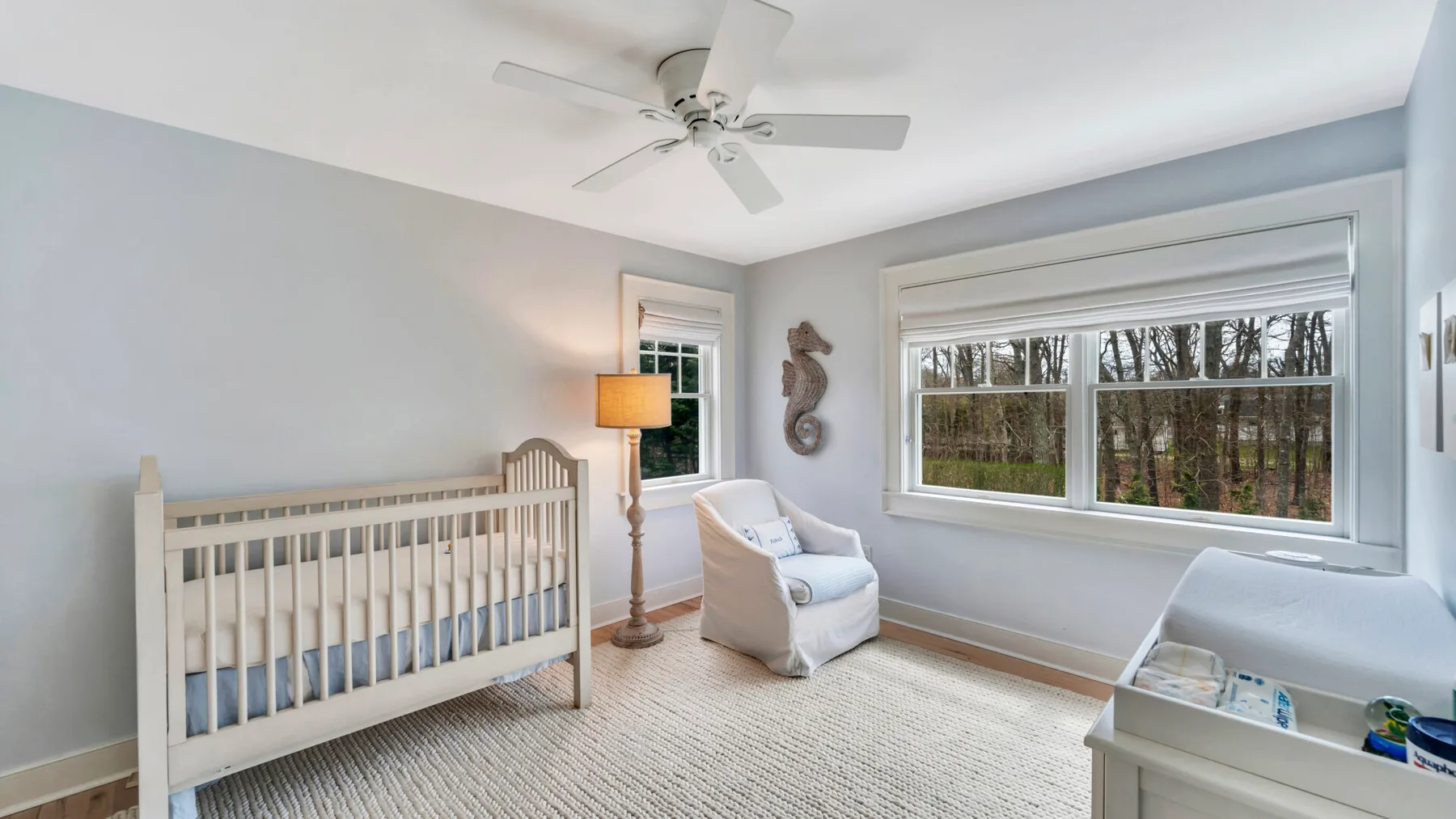 A nursery with a crib and an upholstered seat beside a large window.