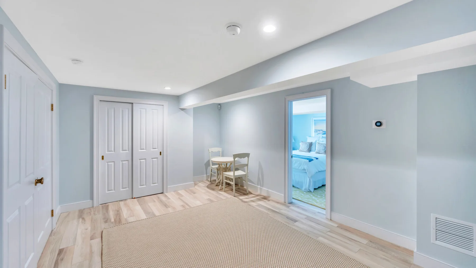 A bright basement room with a small dining table and an open doorway to a bedroom.