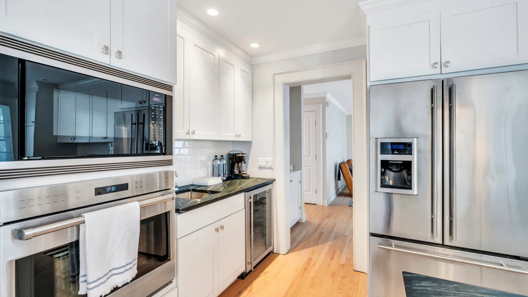 A bright kitchen with white cabinetry, stainless steel appliances, and a central doorway.