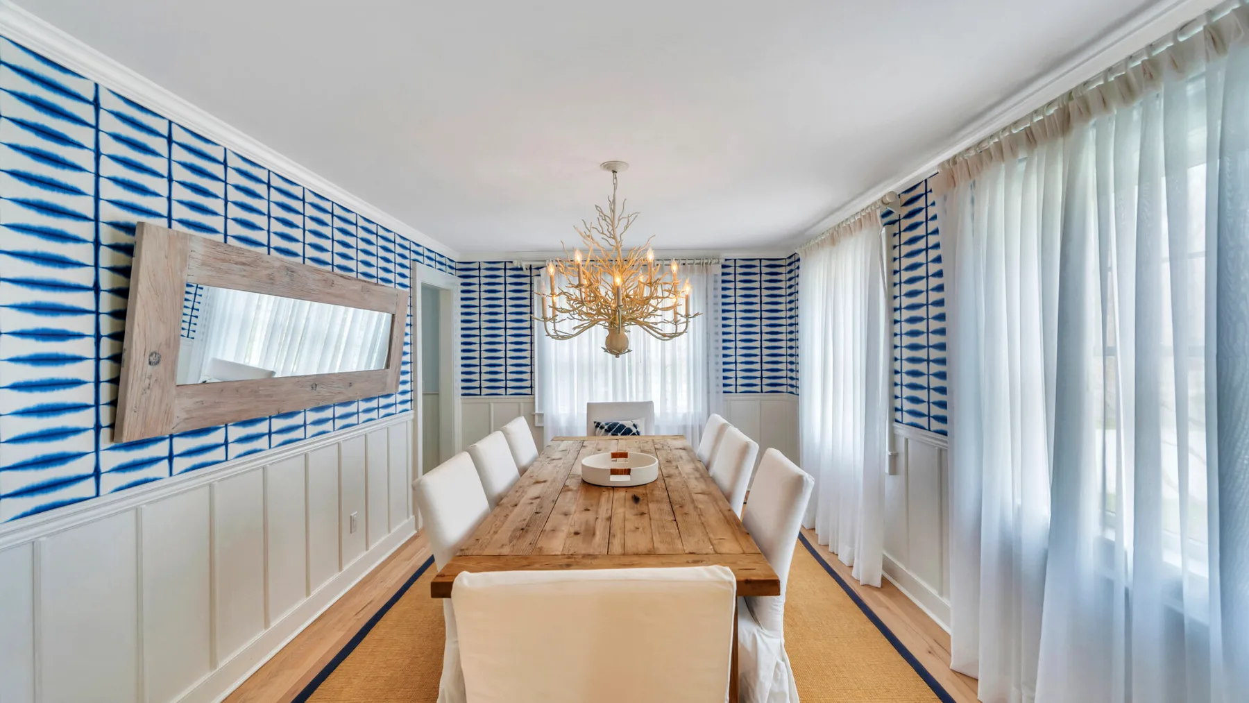 A dining room with a long wooden table, upholstered seating, and patterned wall panels.