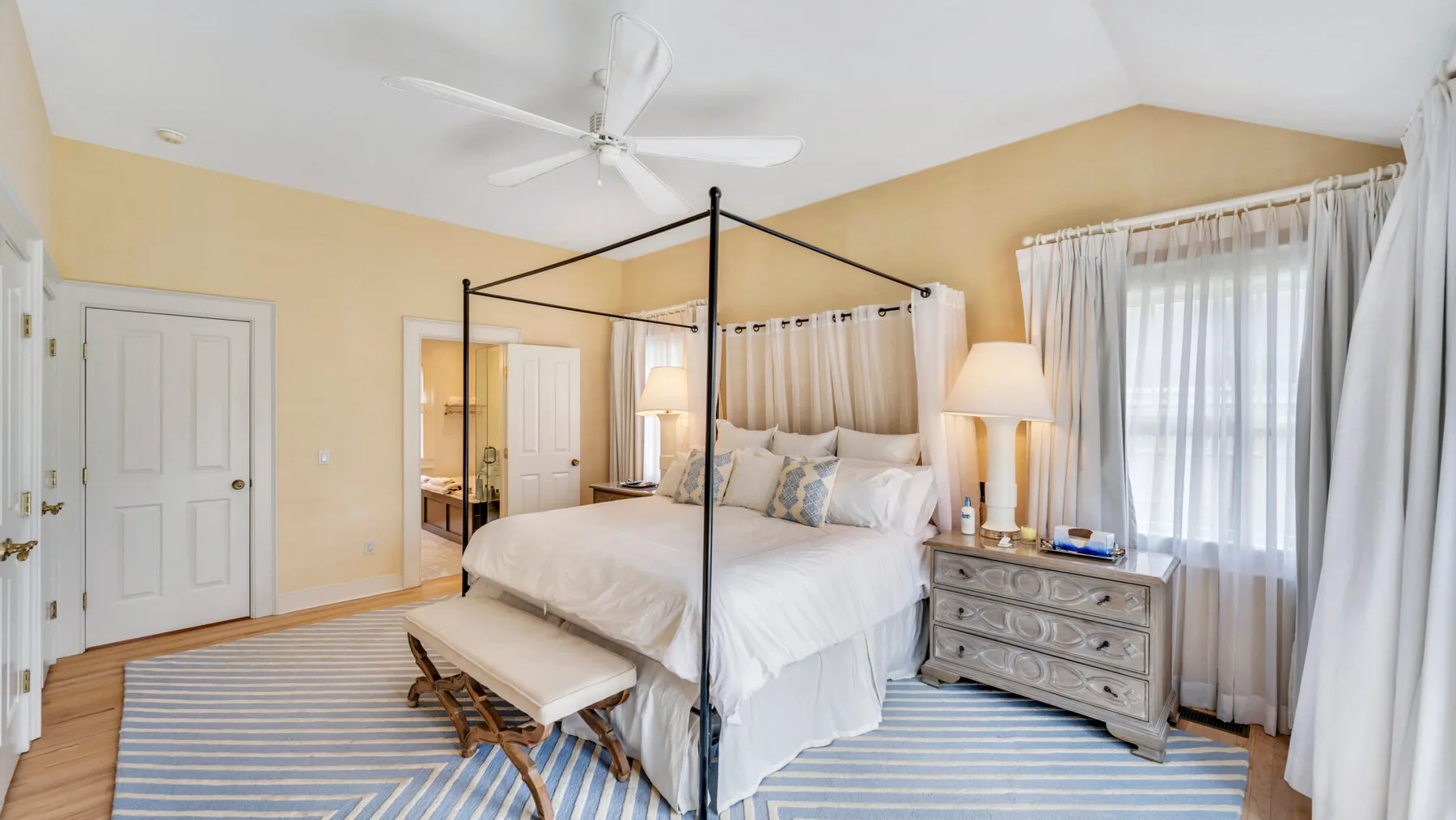 A bright bedroom with a canopy bed and a striped rug.