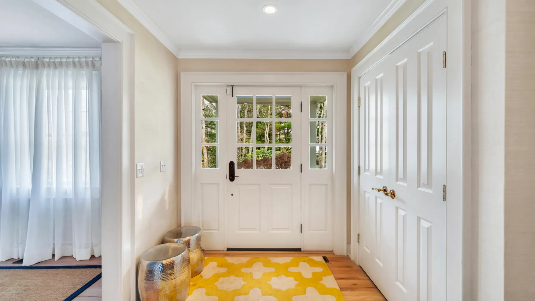 A bright entryway with white paneled doors and a yellow patterned rug.