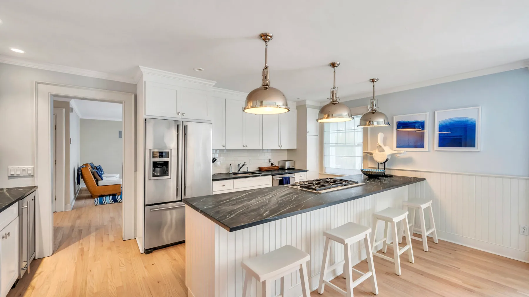 A bright kitchen with a large island, pendant lights, and framed wall art.