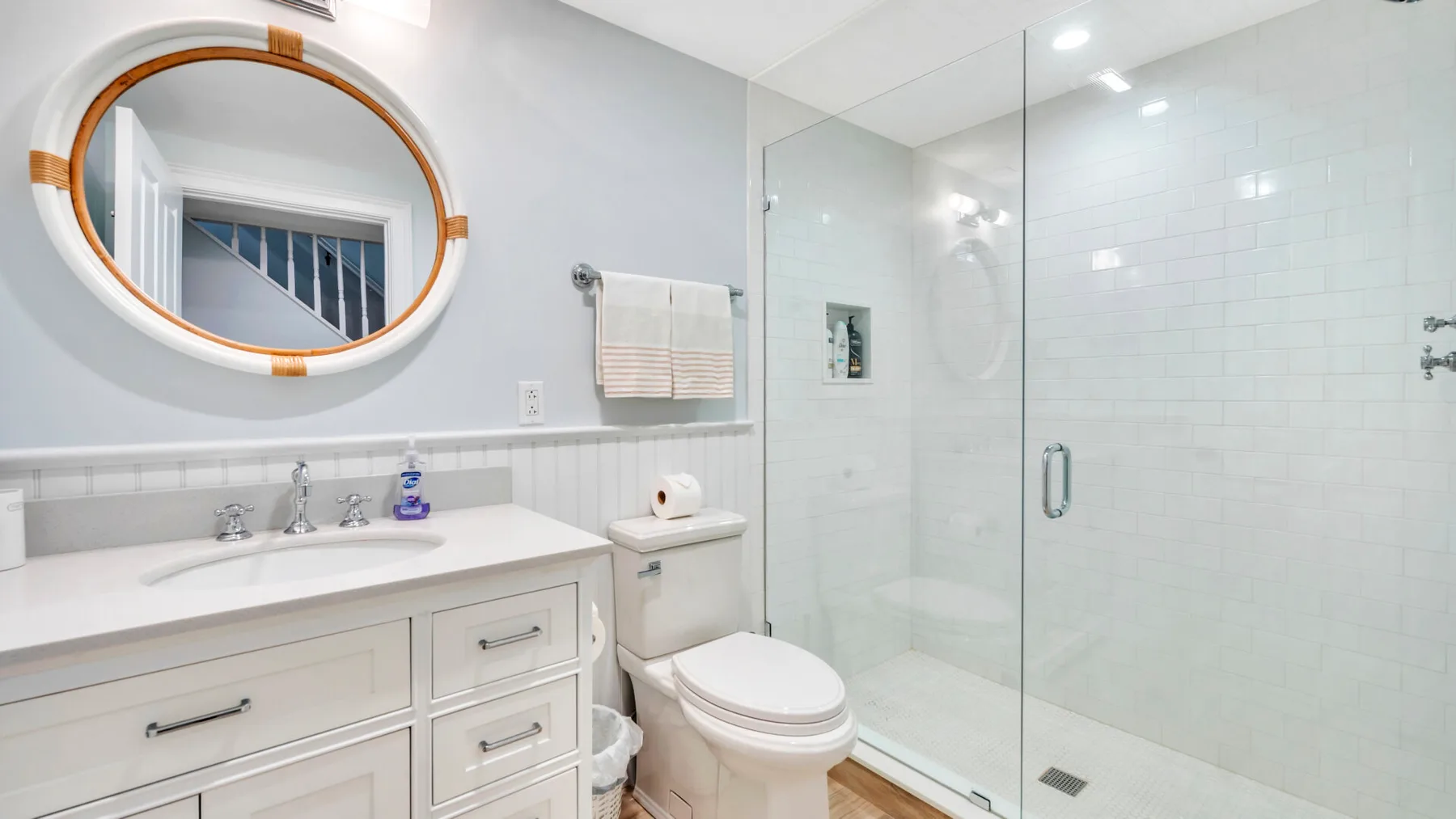A bright bathroom with a vanity, oval mirror, and glass shower.