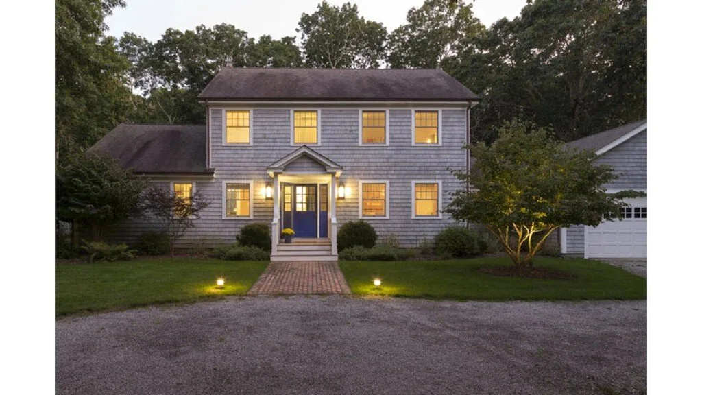 A two-story house with a brick walkway and lit windows at dusk.