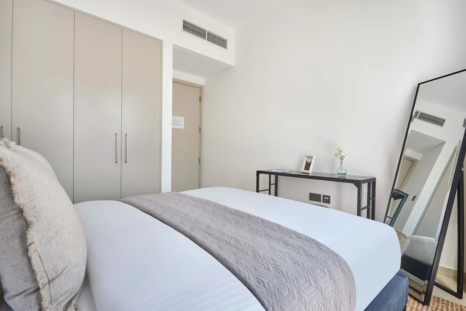 Dormitorio con una cama bien arreglada, armario y espejo de cuerpo entero apoyado.