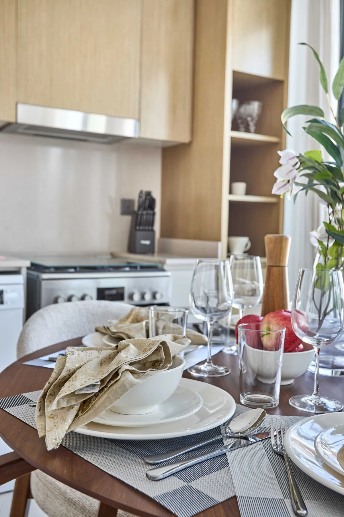 Una mesa puesta con platos y vasos está en una cocina luminosa.