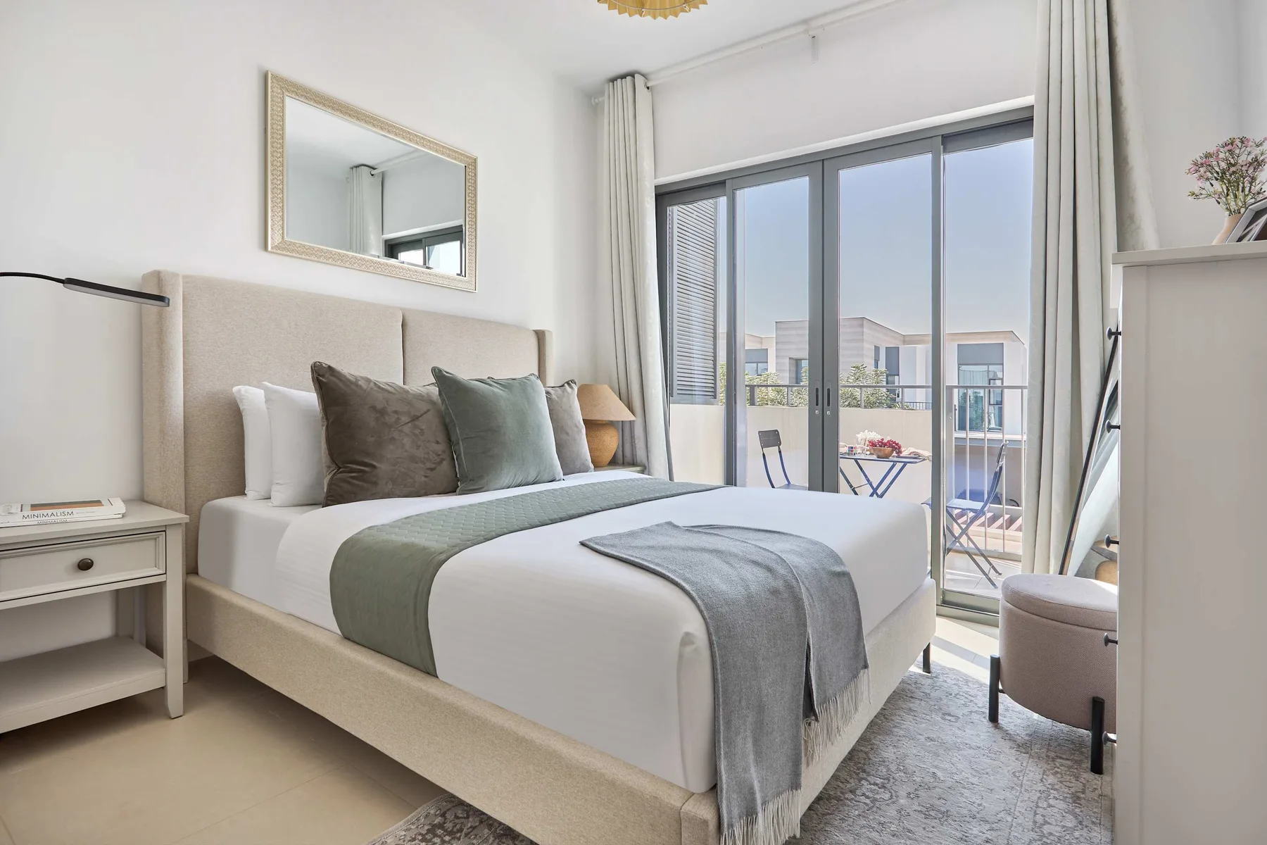 Un dormitorio luminoso con una cama bien hecha y puertas de vidrio que dan a un balcón.