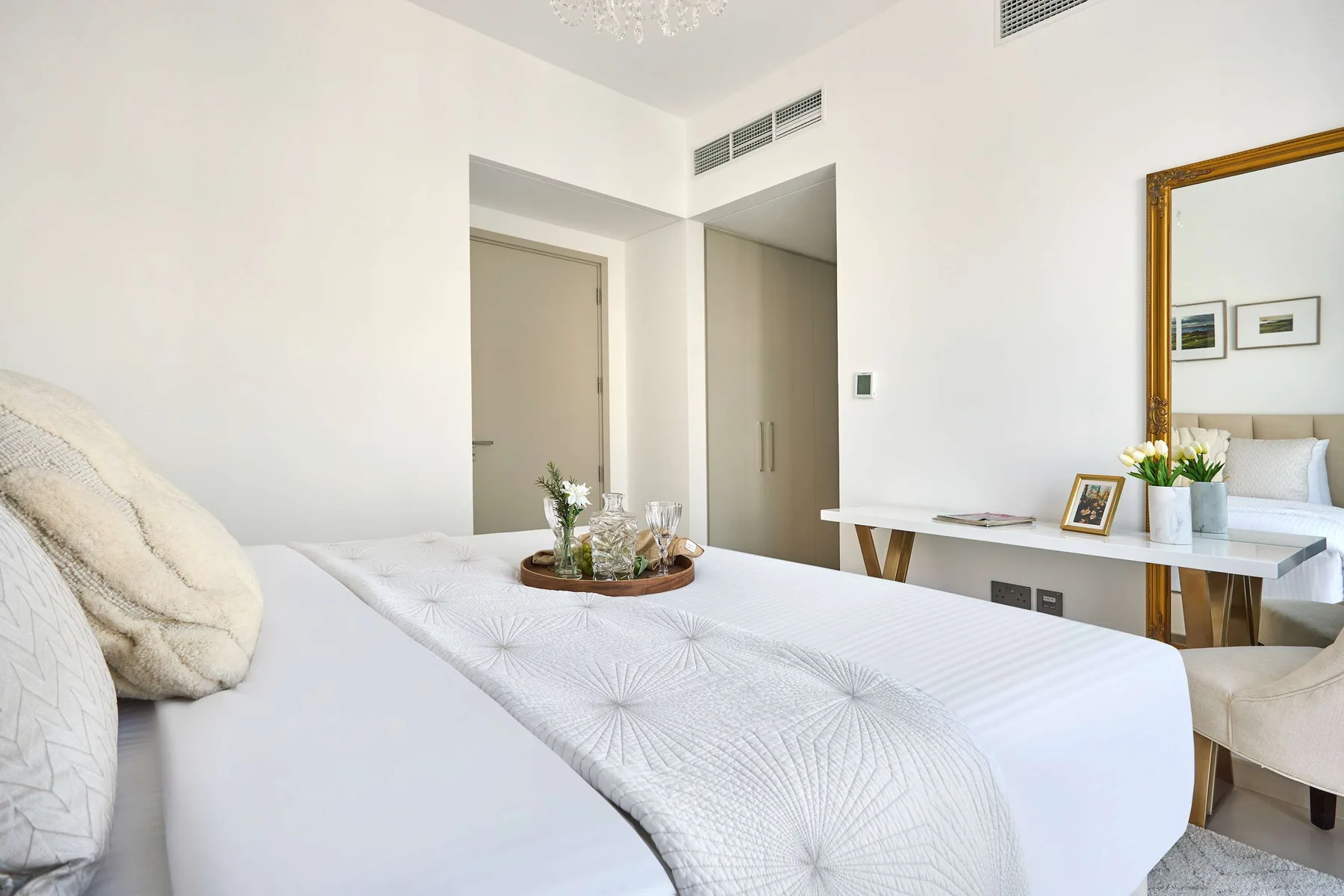 Un dormitorio luminoso con una cama tendida y un escritorio junto al espejo.