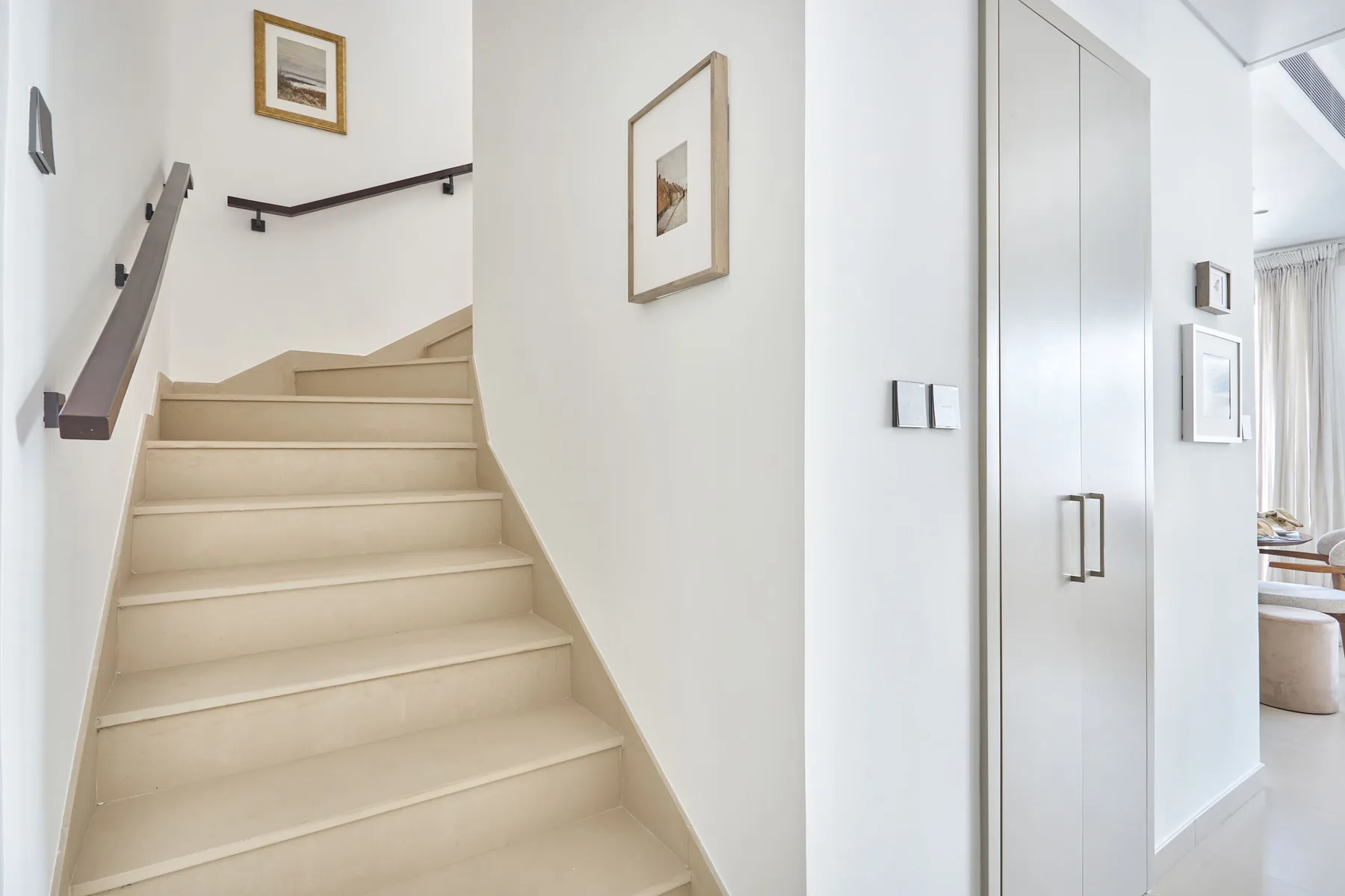 Un pasillo interior luminoso con una escalera y un armario empotrado alto.