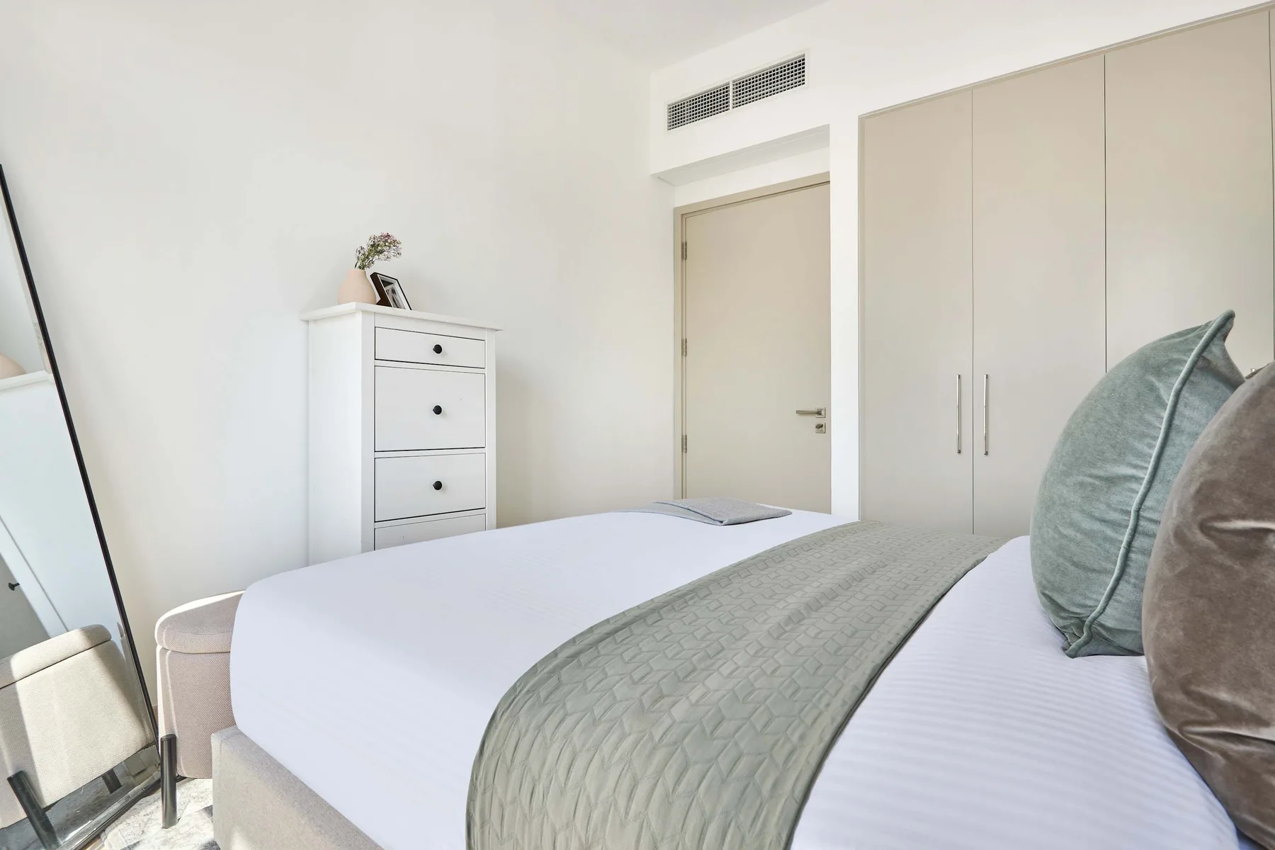 Un dormitorio luminoso con una cama tendida y armarios empotrados.