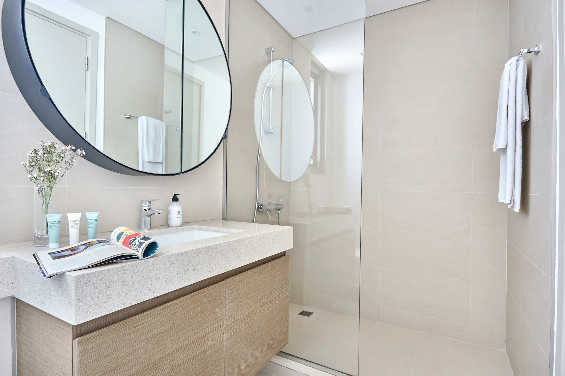 Un baño luminoso con un tocador largo, un espejo grande y una ducha de vidrio.