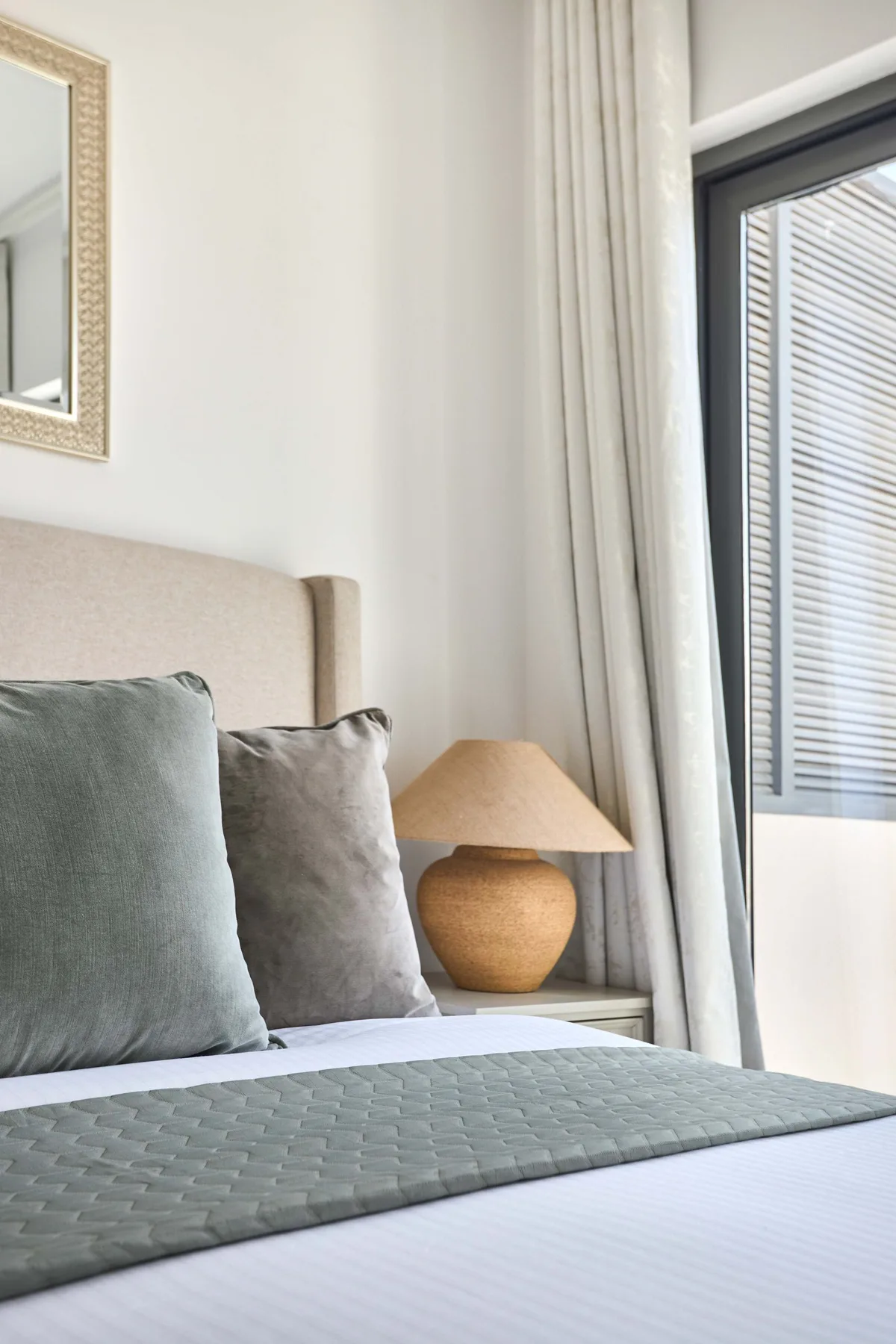 Un dormitorio con una cama tendida, almohadas suaves y una lámpara de noche.