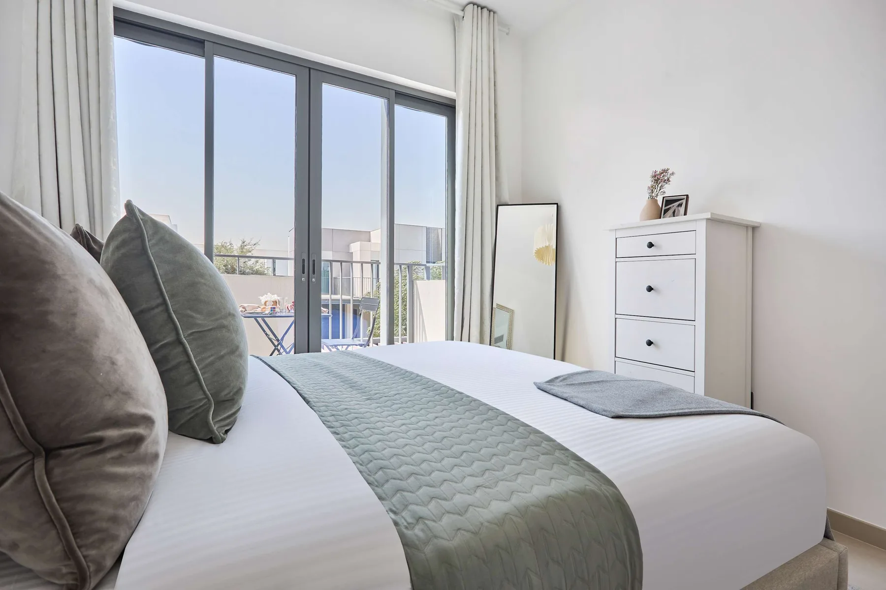 Un dormitorio luminoso con una cama bien tendida junto a grandes ventanas.