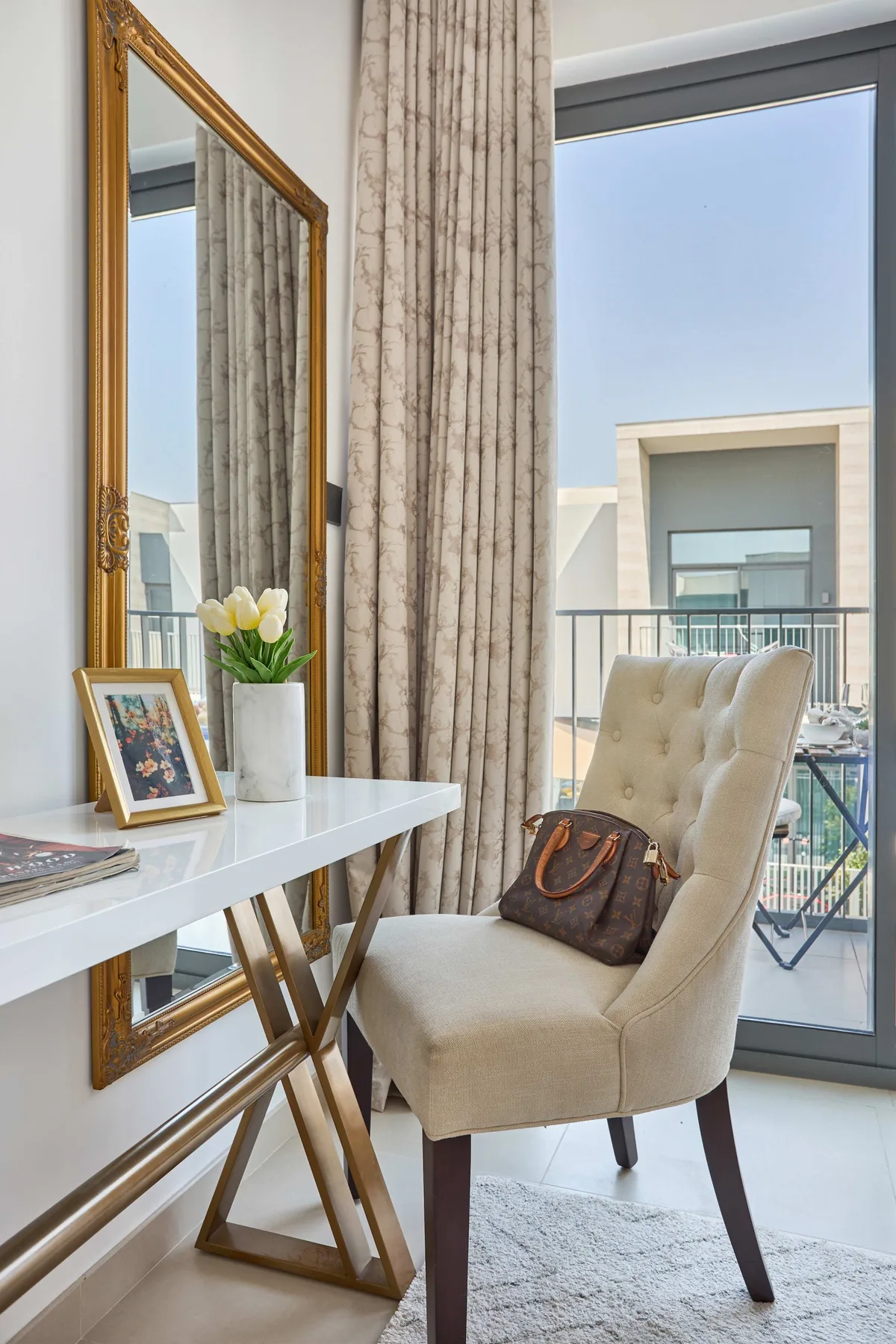 Una zona de estar luminosa con un sillón acolchado junto a una ventana grande con cortinas.