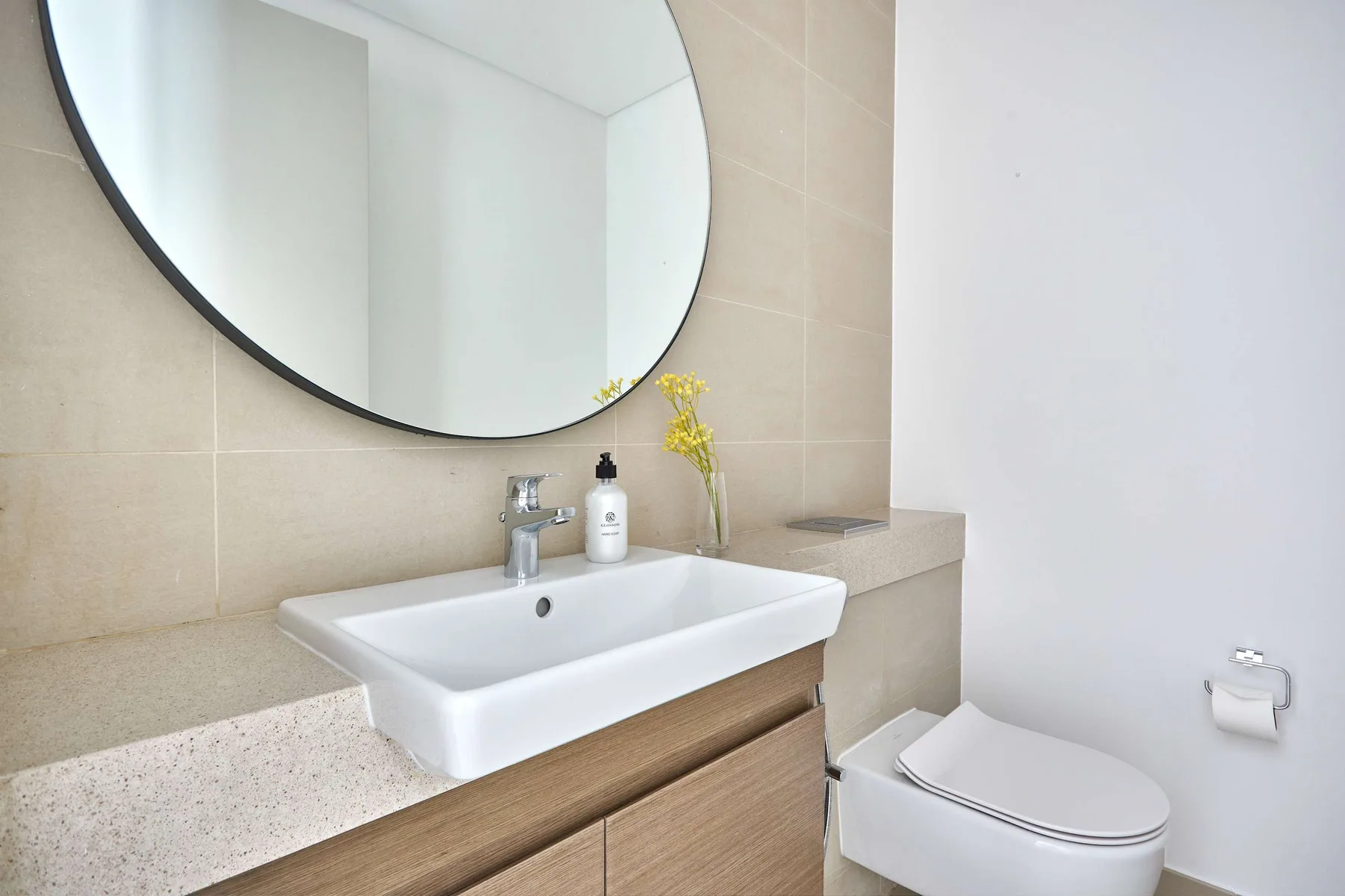 Un baño con lavabo, un espejo redondo grande y un inodoro.