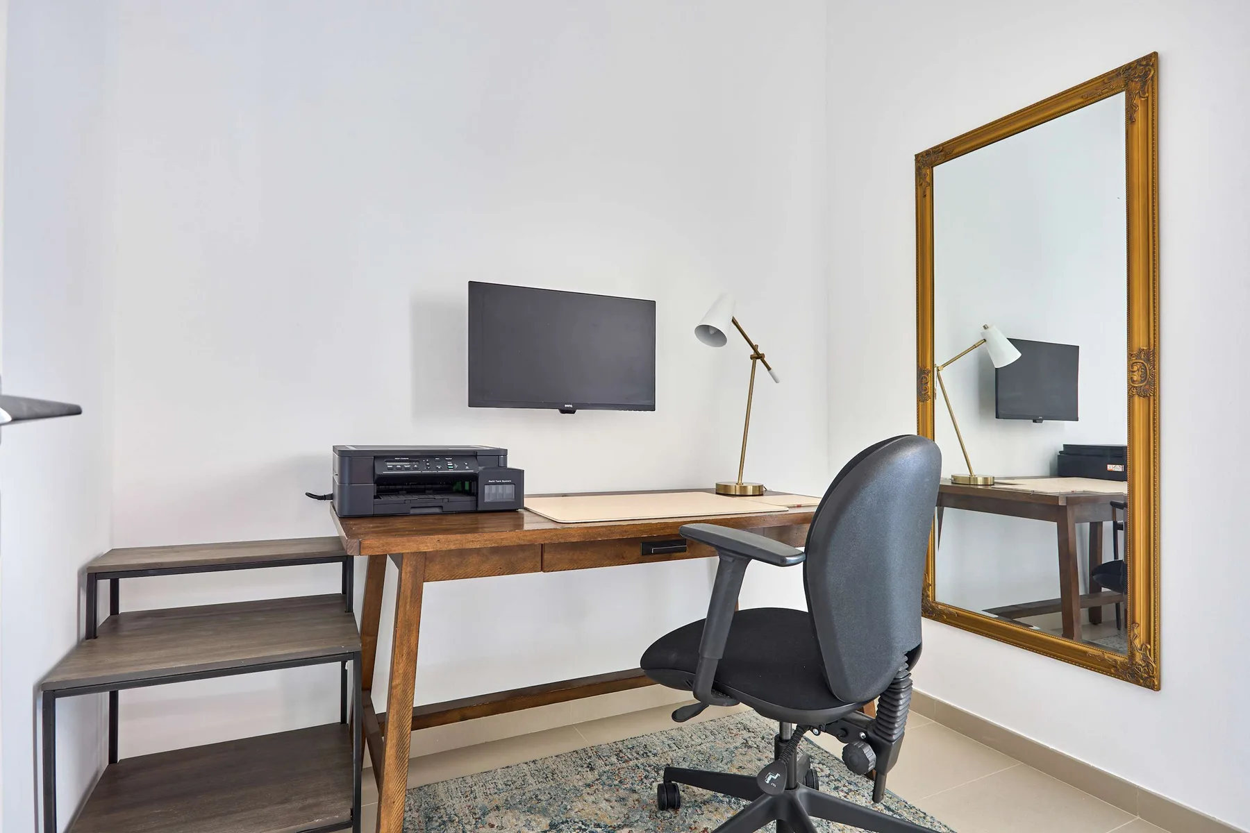 Un despacho en casa con escritorio de madera, monitor y silla con ruedas.