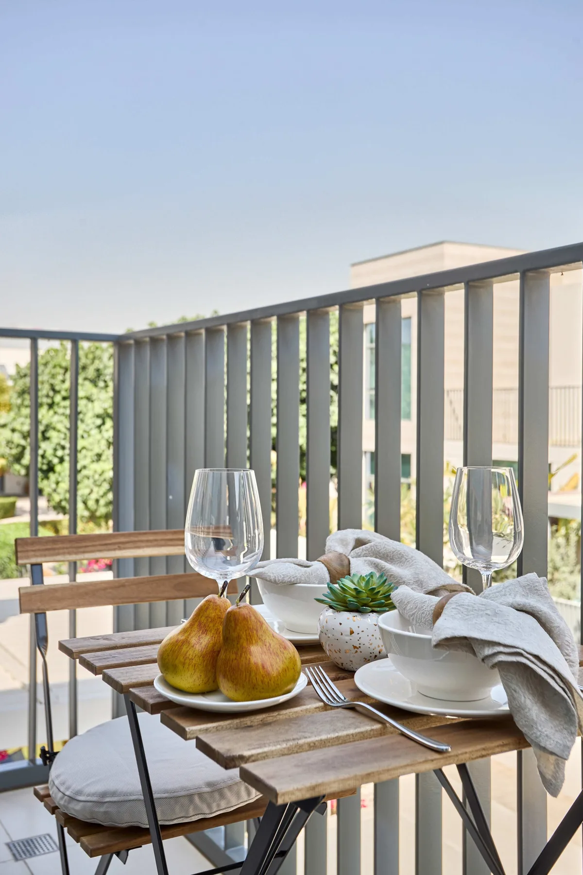 Un pequeño comedor de balcón con una mesa de madera preparada con peras y platos.