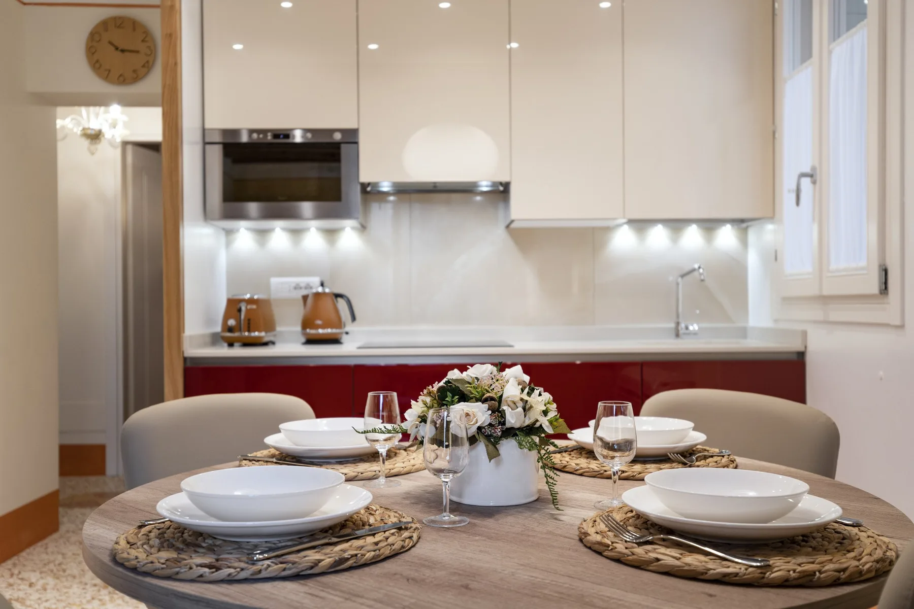 Una mesa puesta con platos y flores está frente a una cocina luminosa.