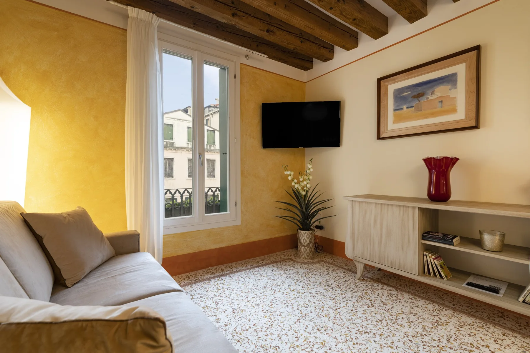Una sala de estar con asientos, un televisor en la pared y un mueble.