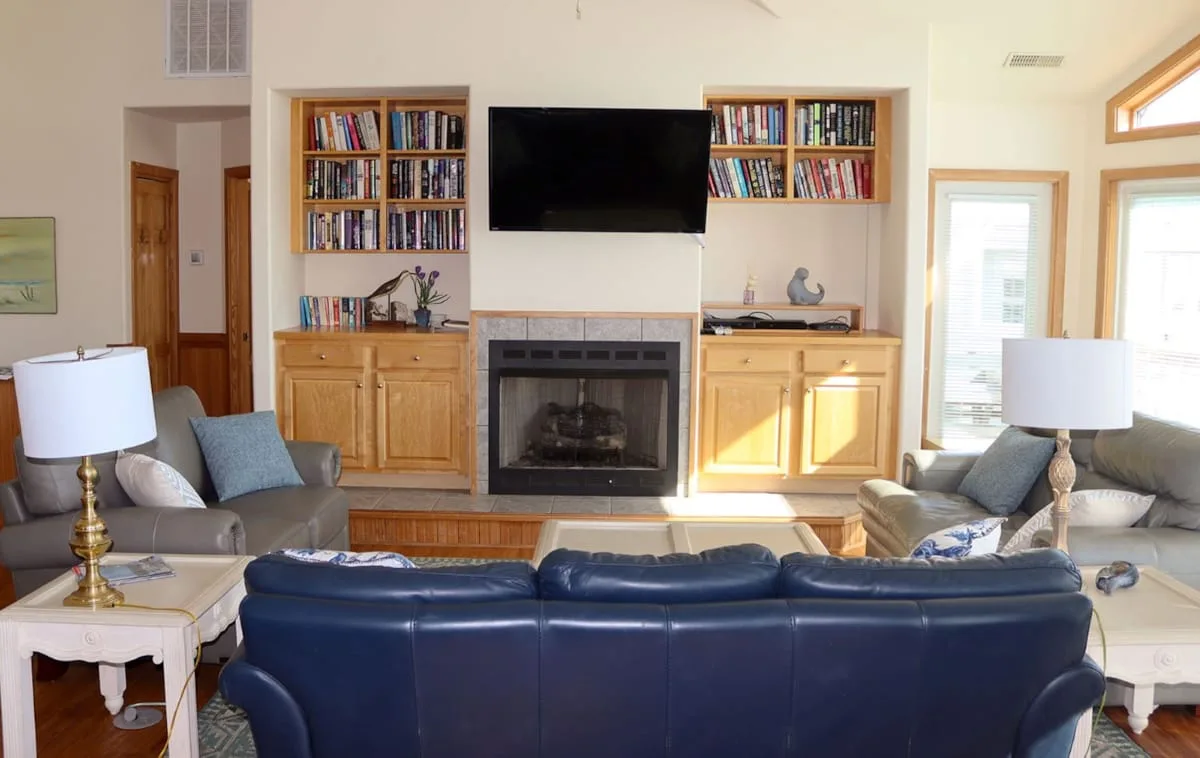 Una sala de estar con asientos azules frente a una chimenea y un televisor en la pared.