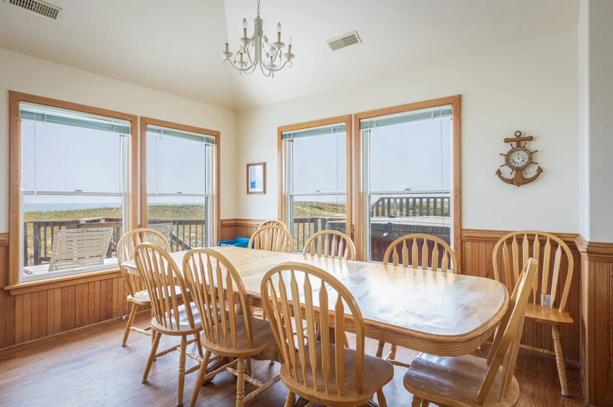 A bright dining room with a large table and wooden seating beside wide windows.