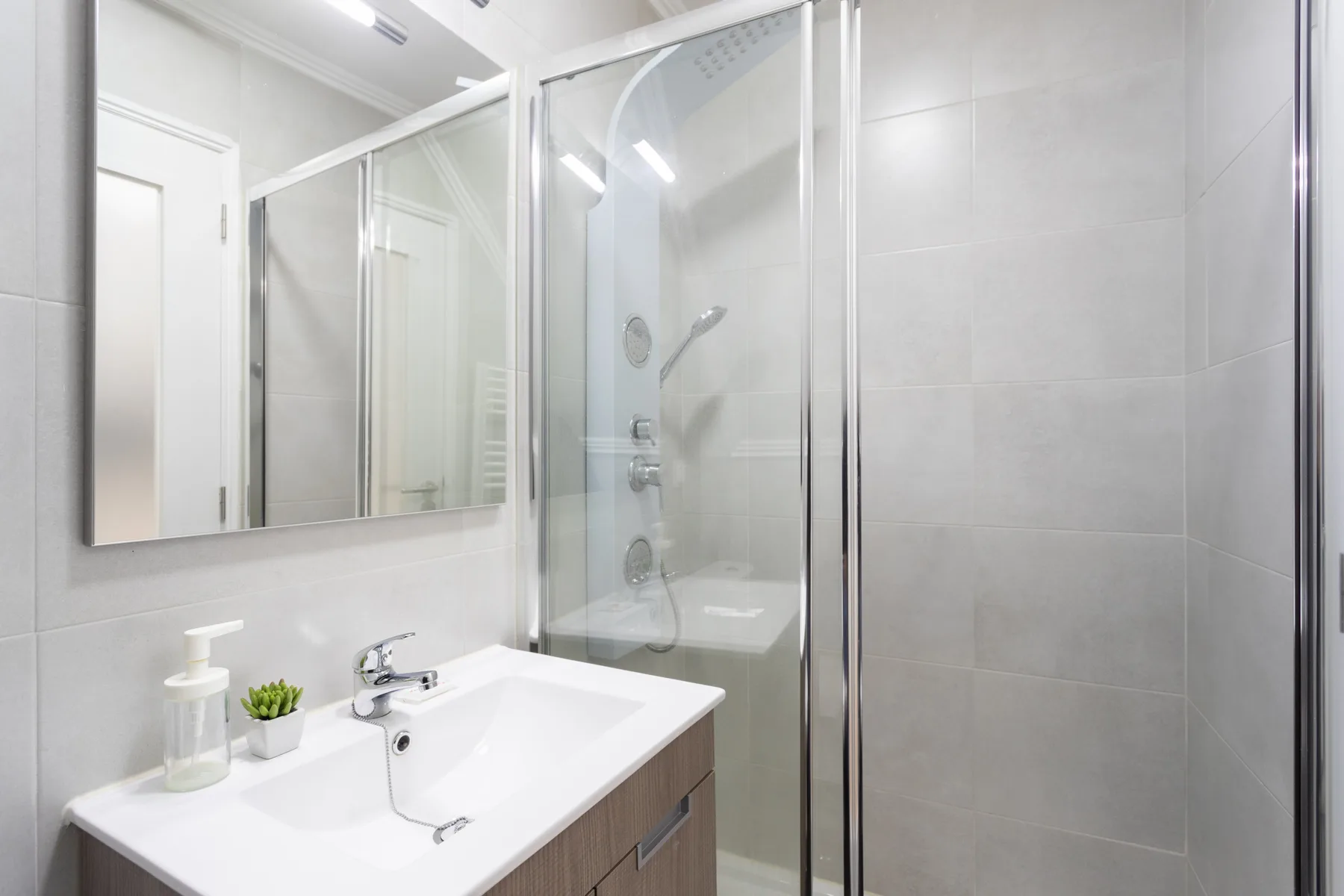 Un baño con lavabo, espejo y ducha con mampara de vidrio.