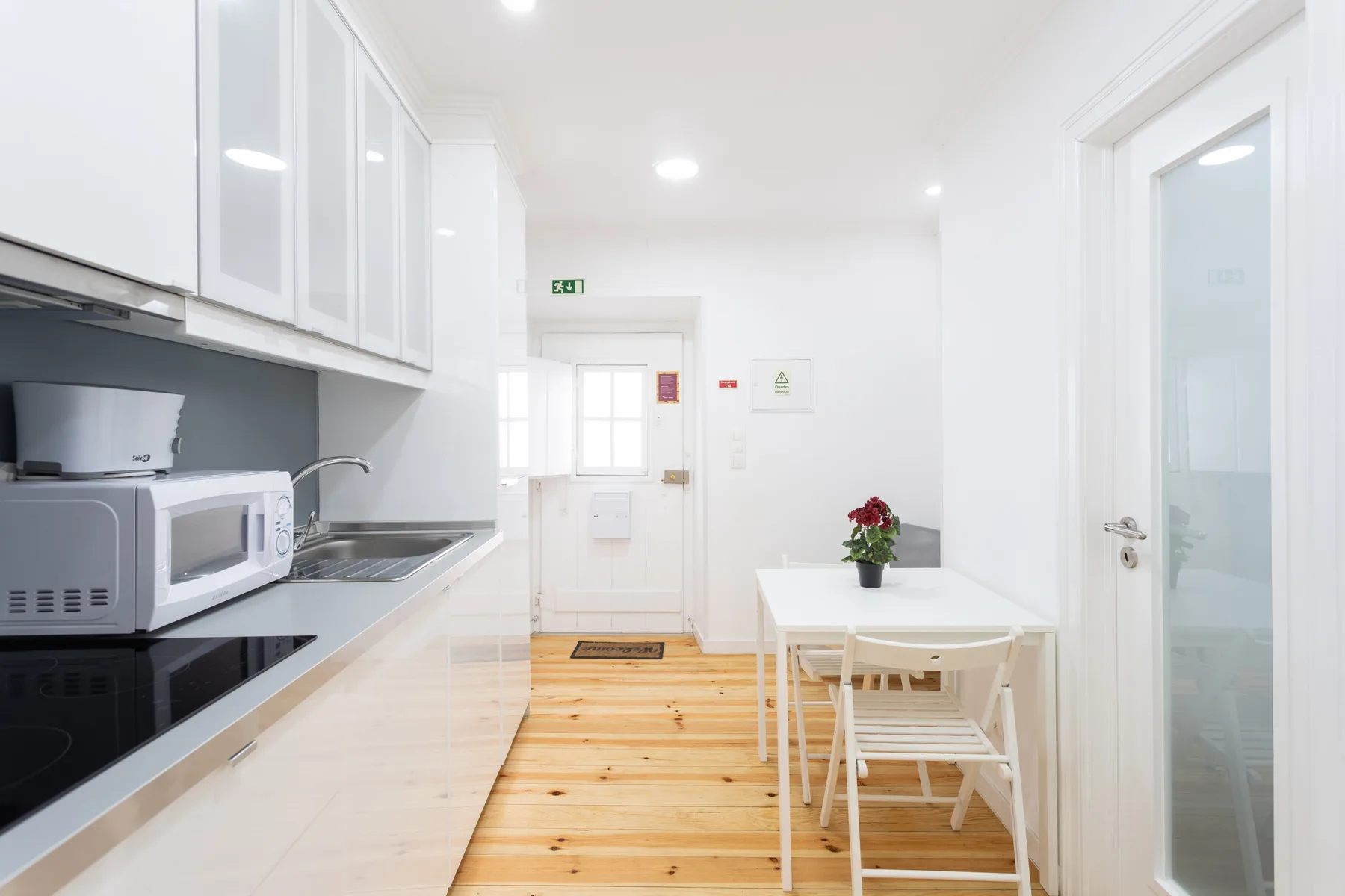 Una cocina luminosa con zona de comedor, muebles blancos y suelo de madera.