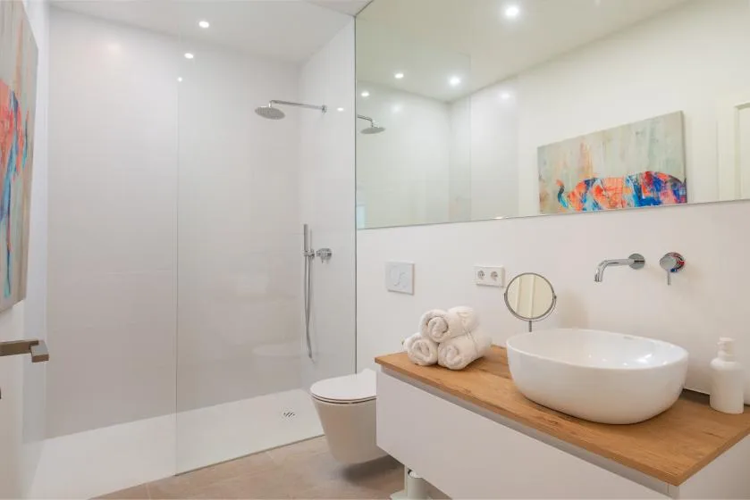 Un baño luminoso con ducha, inodoro y un mueble con lavabo sobre encimera.
