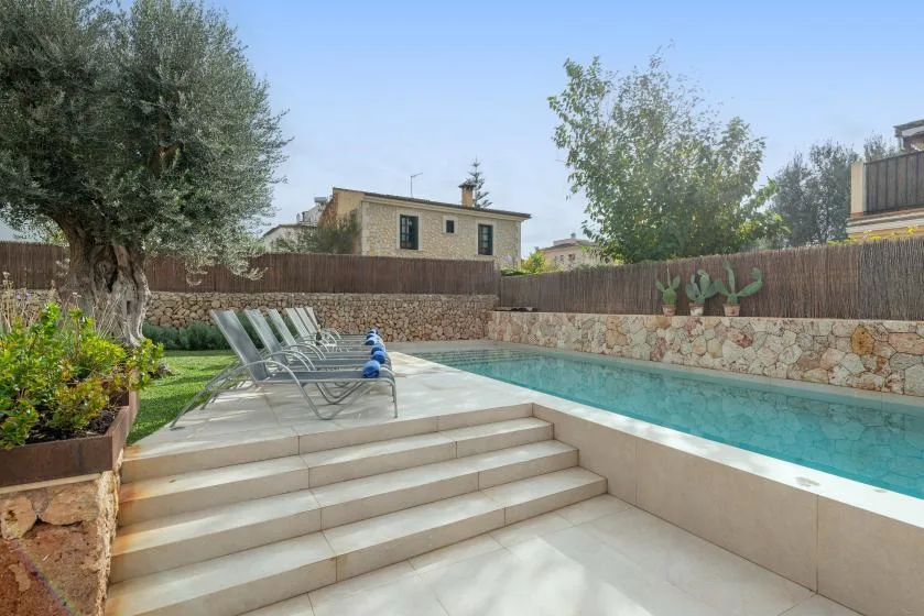 Una piscina al aire libre junto a un patio pavimentado y un jardín.