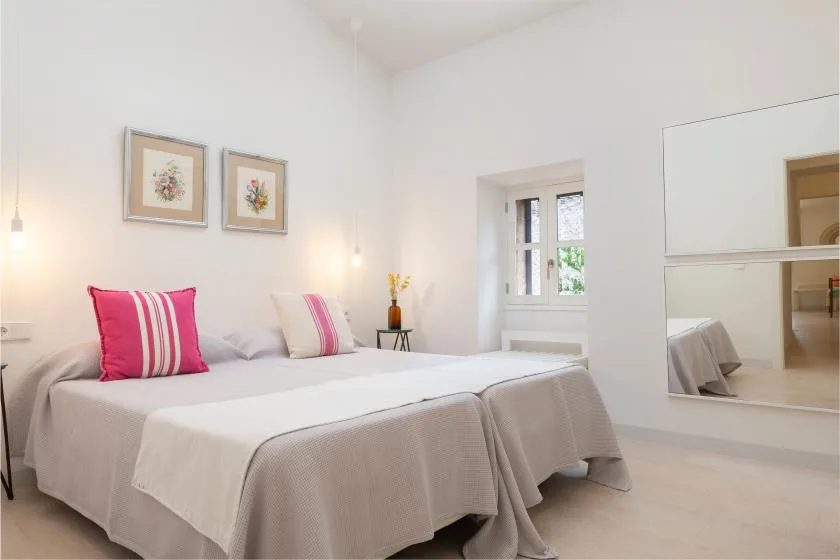 Un dormitorio luminoso con una cama doble, cojines de colores y láminas florales enmarcadas.