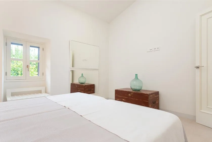 Un dormitorio luminoso con una cama tendida y una pequeña cómoda de madera.