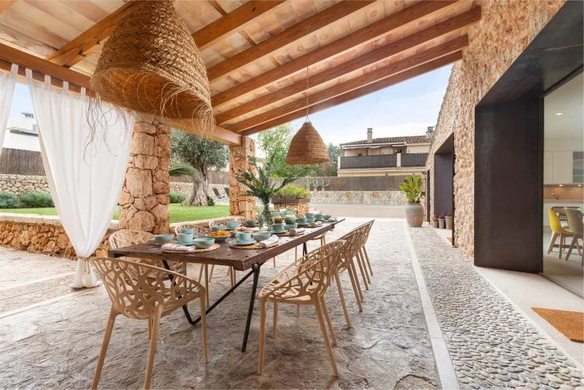 Una zona de comedor exterior cubierta con una mesa larga bajo vigas de madera vistas.