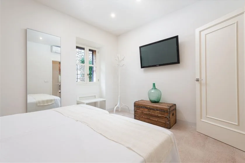 Un dormitorio luminoso con una cama, un televisor en la pared y una cómoda de madera.