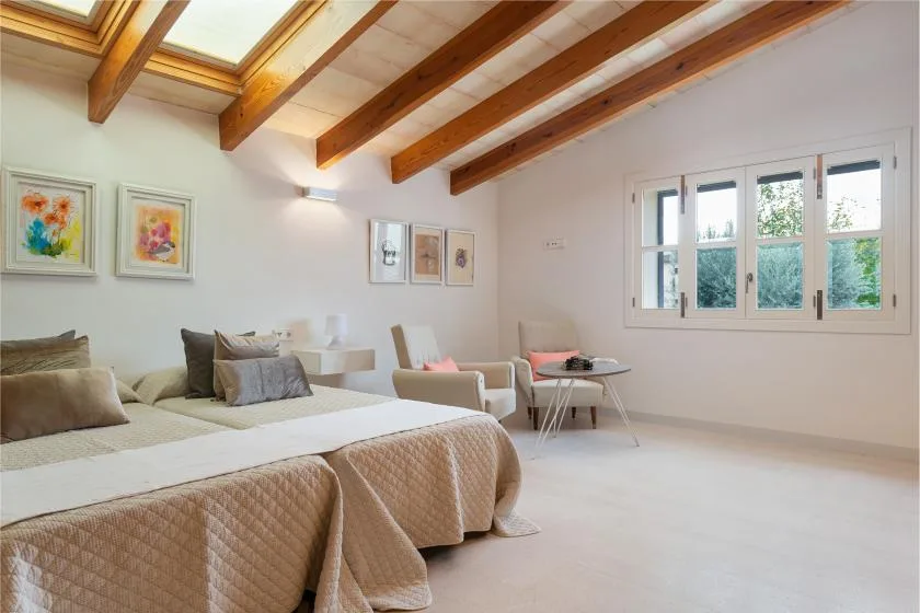 Un dormitorio luminoso con camas, asientos y vigas de madera expuestas en el techo.