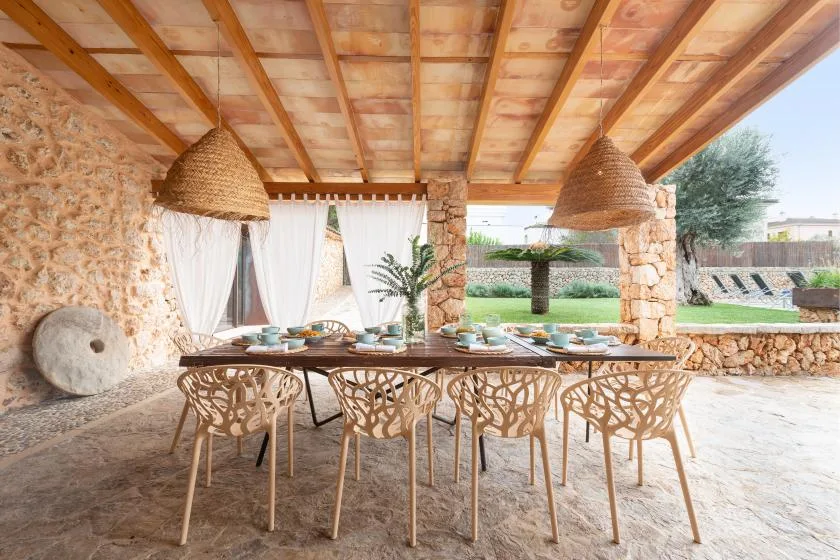 Comedor exterior cubierto con una mesa larga y asientos tejidos.