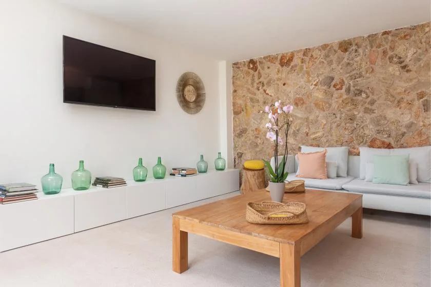 Una sala de estar con mesa de centro de madera, televisor en la pared y pared de piedra.