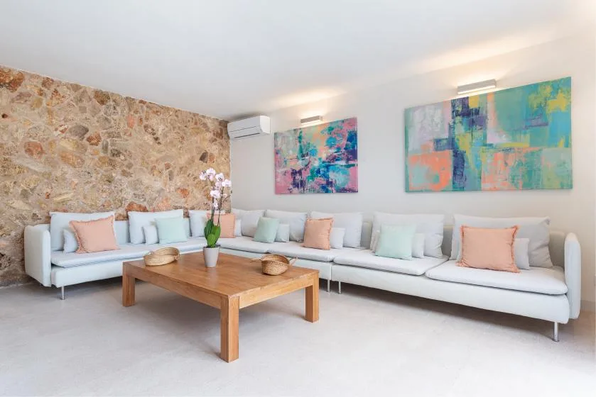 Una sala luminosa con asientos blancos, una mesa de centro de madera y arte abstracto colorido.