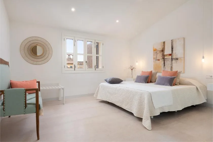 Un dormitorio luminoso con una cama grande, cojines de colores y una ventana.