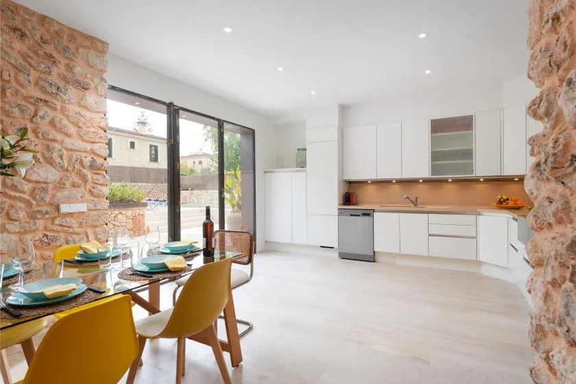 Una cocina y comedor luminosos con gabinetes blancos y una mesa de madera.